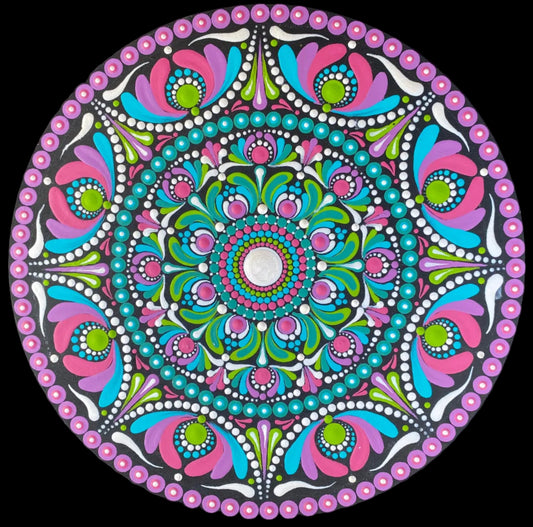 A circular mandala art piece with a vibrant multicolor design featuring pink, teal, green, and white patterns, displayed on a black background.
